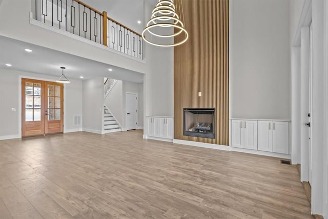 unfurnished living room featuring light wood finished floors, stairs, french doors, a fireplace, and a notable chandelier