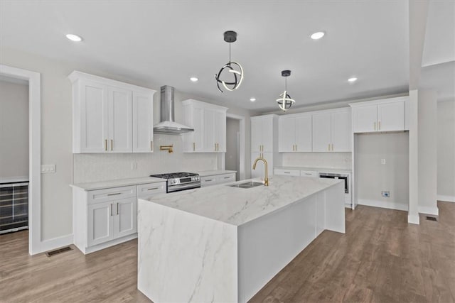 kitchen featuring wall chimney exhaust hood, a kitchen island with sink, white cabinets, and a sink