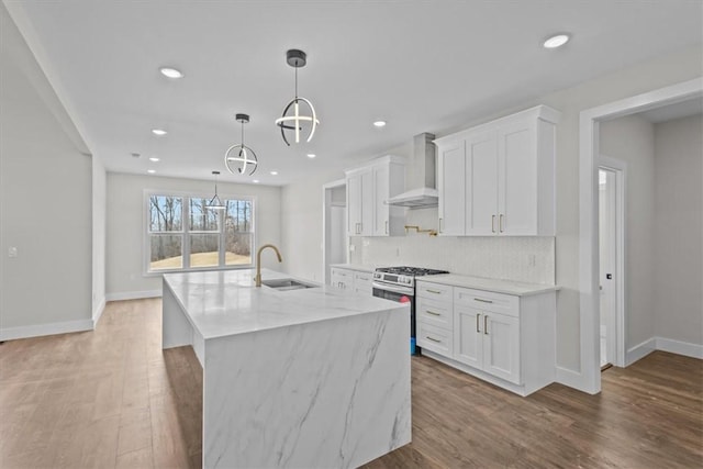 kitchen with decorative light fixtures, white cabinetry, a sink, stainless steel gas range, and wall chimney exhaust hood