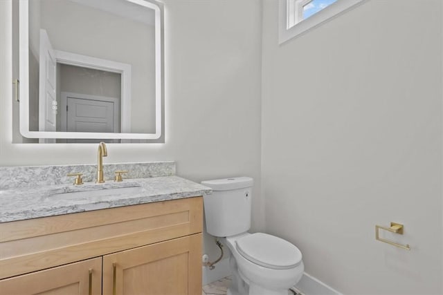 half bath featuring toilet, marble finish floor, vanity, and baseboards