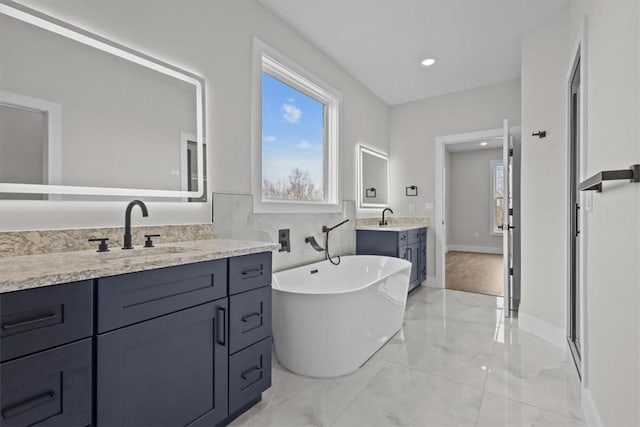 bathroom with a soaking tub, marble finish floor, two vanities, and a sink