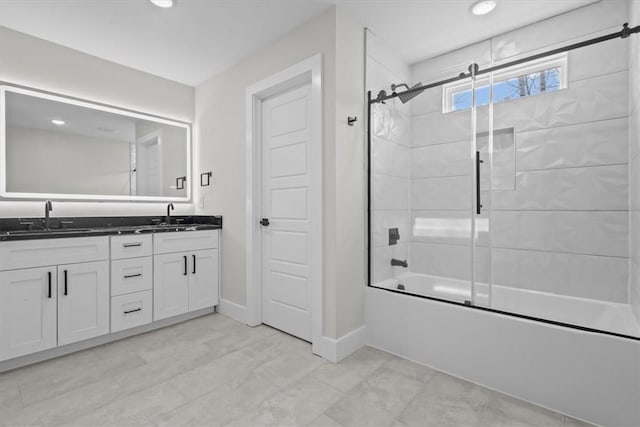 full bath with double vanity, baseboards, bath / shower combo with glass door, and a sink