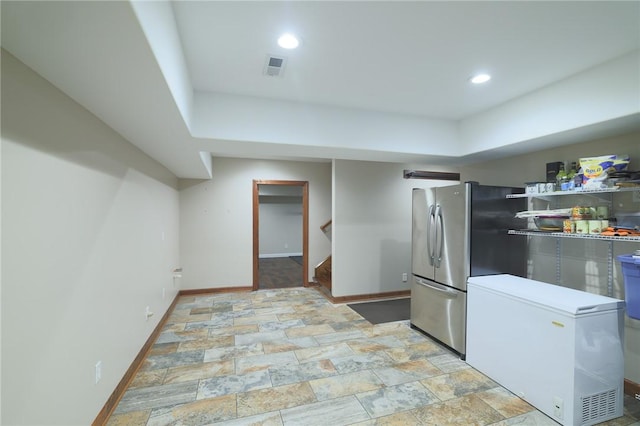 kitchen with stone finish flooring, visible vents, baseboards, and fridge