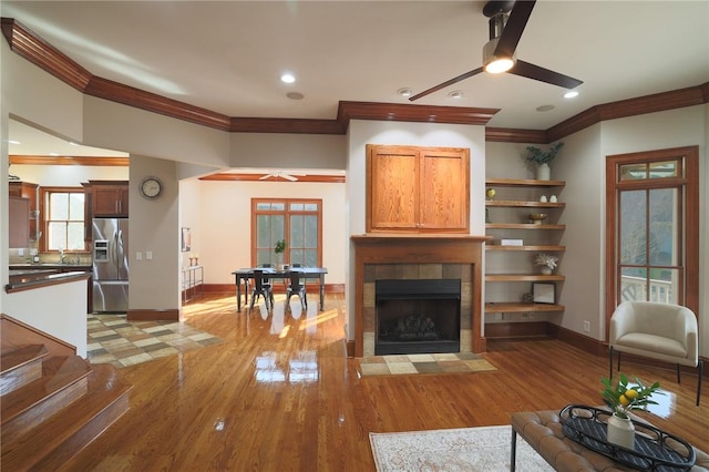 living room featuring a tile fireplace, ceiling fan, and light wood finished floors