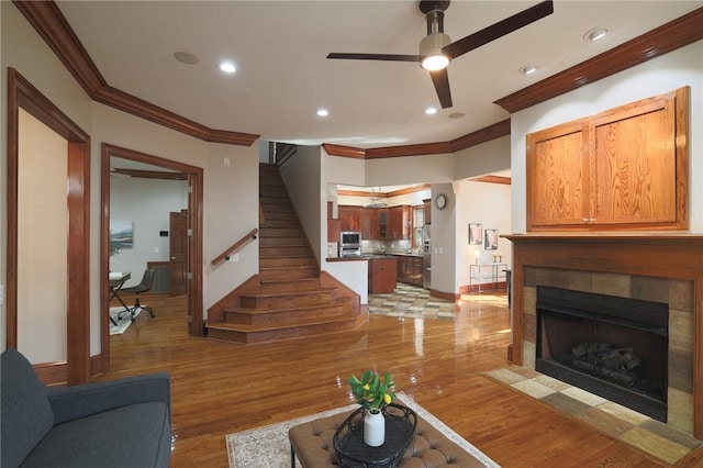 living room with crown molding, a fireplace, stairway, and light wood finished floors