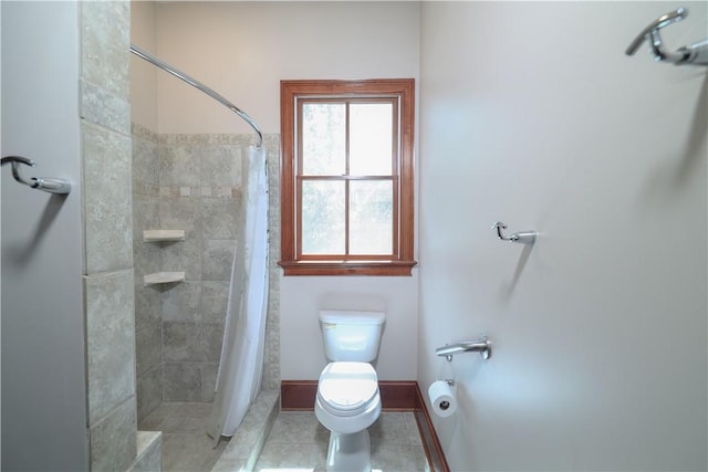 bathroom with tile patterned flooring, baseboards, tiled shower, and toilet