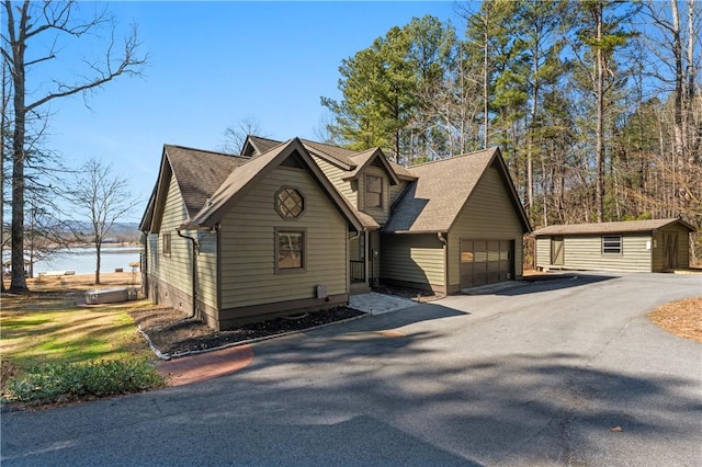 chalet / cabin featuring a garage, an outbuilding, a water view, and roof with shingles