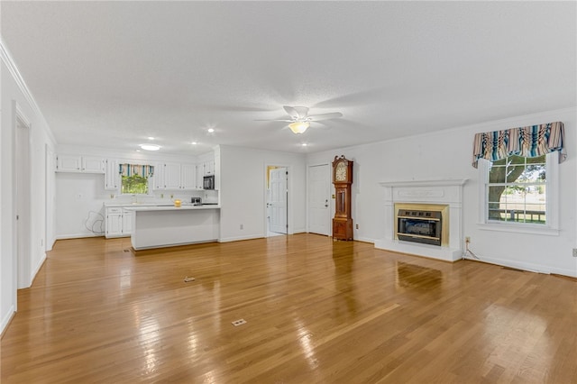 unfurnished living room with baseboards, a glass covered fireplace, light wood-style flooring, ceiling fan, and a textured ceiling