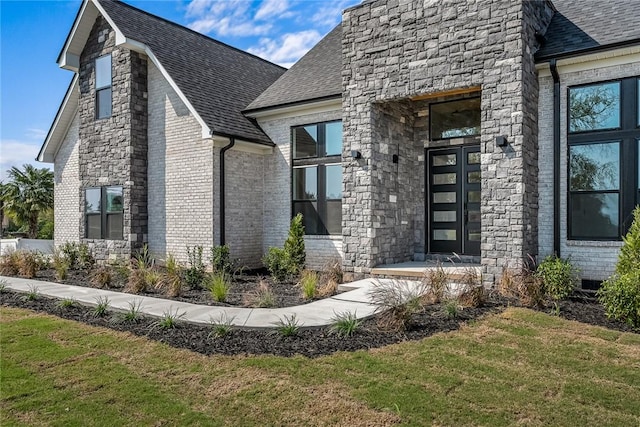 entrance to property with brick siding, roof with shingles, and a lawn