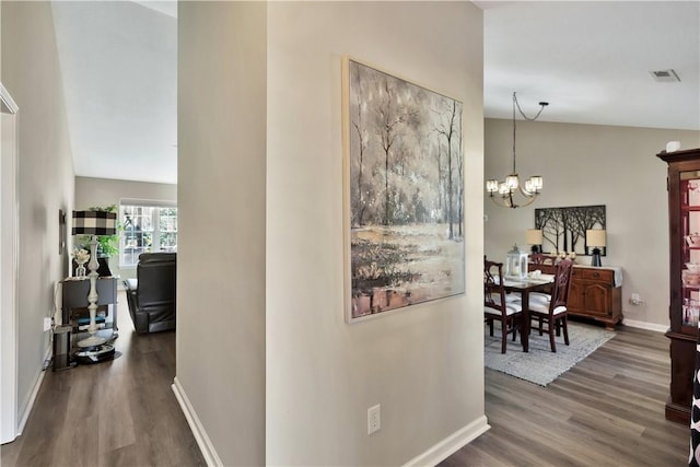 hall featuring a chandelier, visible vents, baseboards, and wood finished floors