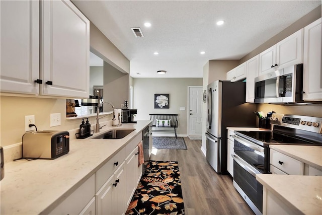 kitchen featuring visible vents, appliances with stainless steel finishes, white cabinets, a sink, and wood finished floors