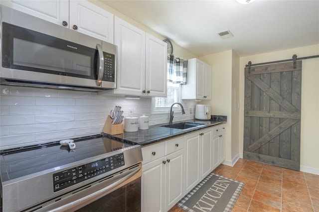 kitchen featuring backsplash, a barn door, appliances with stainless steel finishes, white cabinetry, and a sink