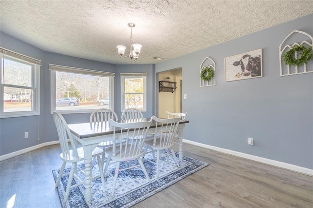 dining space featuring a chandelier, a textured ceiling, wood finished floors, and baseboards