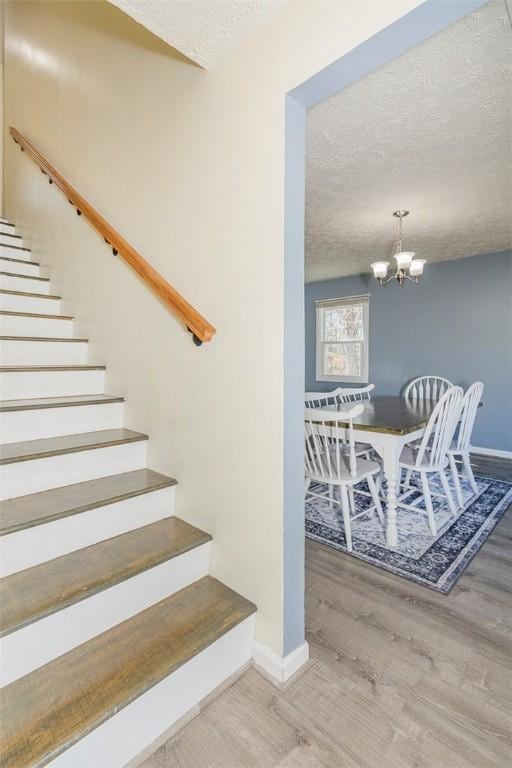 stairway featuring a notable chandelier, a textured ceiling, baseboards, and wood finished floors