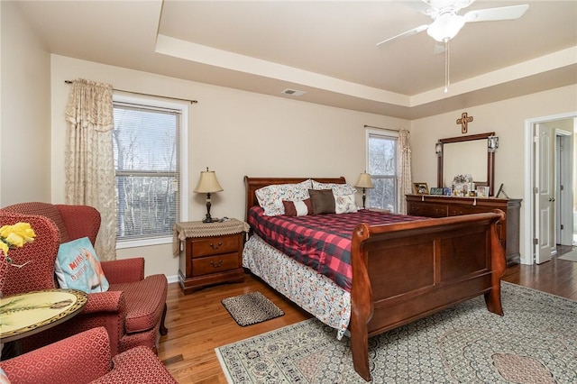 bedroom featuring a tray ceiling, visible vents, and wood finished floors