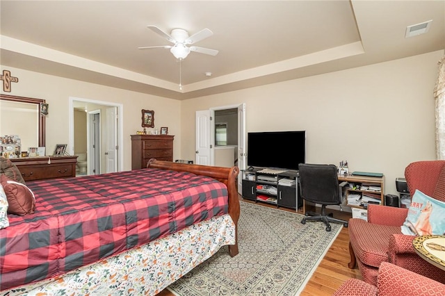 bedroom with visible vents, a tray ceiling, ceiling fan, and wood finished floors