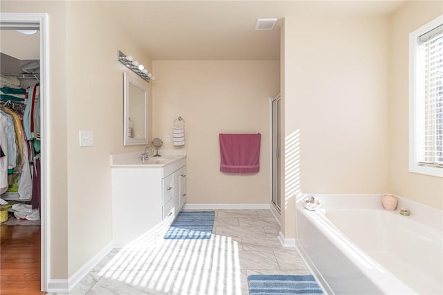 full bathroom with a garden tub, a spacious closet, a stall shower, vanity, and baseboards