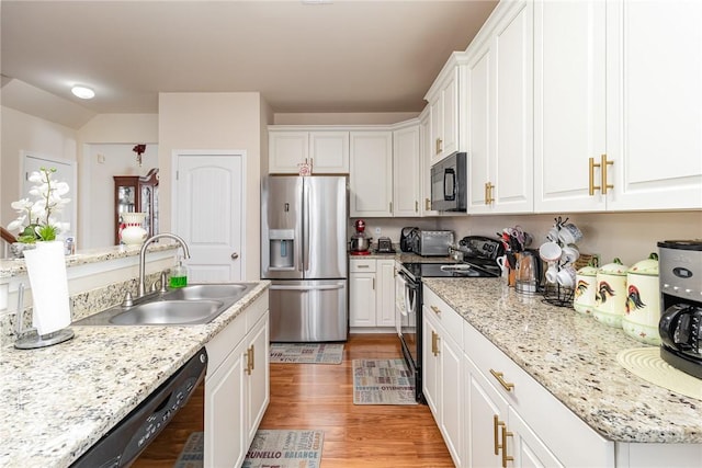 kitchen with light stone counters, a sink, light wood-style floors, white cabinets, and black appliances