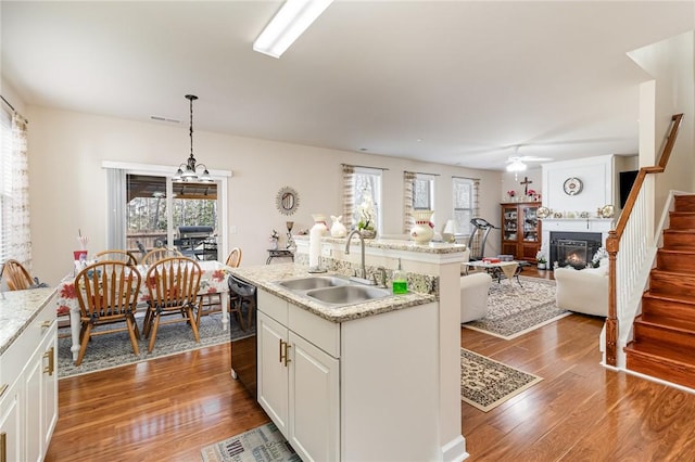 kitchen with black dishwasher, dark wood-style floors, a lit fireplace, pendant lighting, and a sink