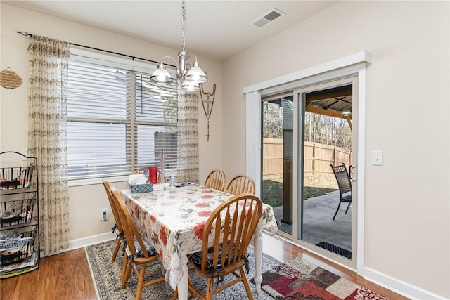 dining area featuring a notable chandelier, baseboards, visible vents, and wood finished floors