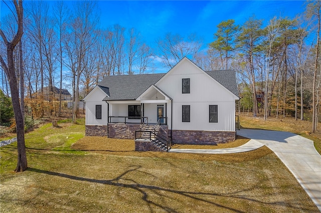 modern farmhouse featuring covered porch, driveway, a front lawn, and roof with shingles