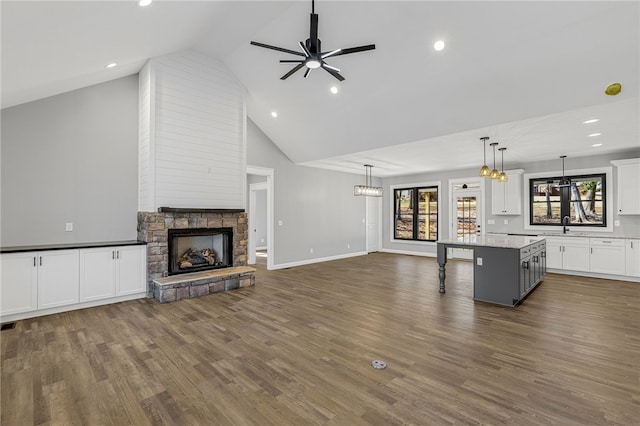 unfurnished living room with a ceiling fan, dark wood finished floors, a sink, and a stone fireplace