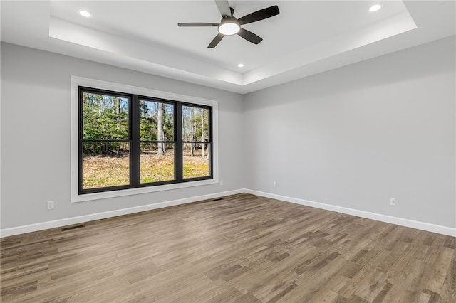 unfurnished room with recessed lighting, a raised ceiling, visible vents, wood finished floors, and baseboards