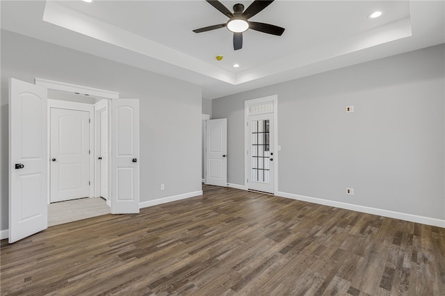 unfurnished bedroom featuring baseboards, a tray ceiling, wood finished floors, and recessed lighting