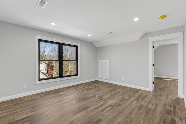 empty room featuring lofted ceiling, wood finished floors, visible vents, and baseboards