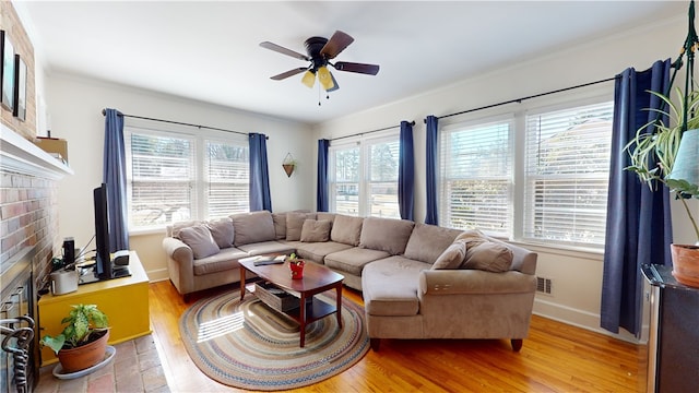 living room featuring visible vents, baseboards, a ceiling fan, light wood-style flooring, and a brick fireplace