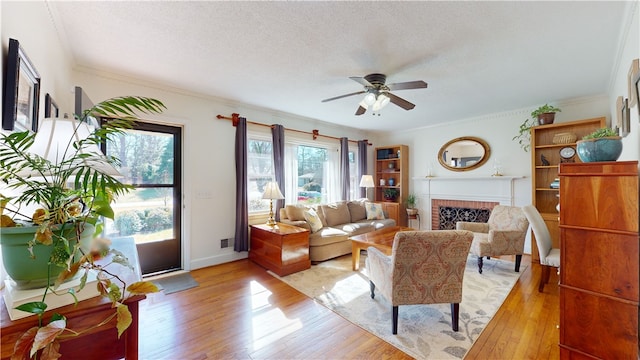 living room with a textured ceiling, ceiling fan, a fireplace, light wood-type flooring, and crown molding