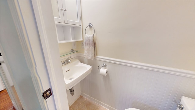 half bath featuring wainscoting, a sink, and tile patterned floors