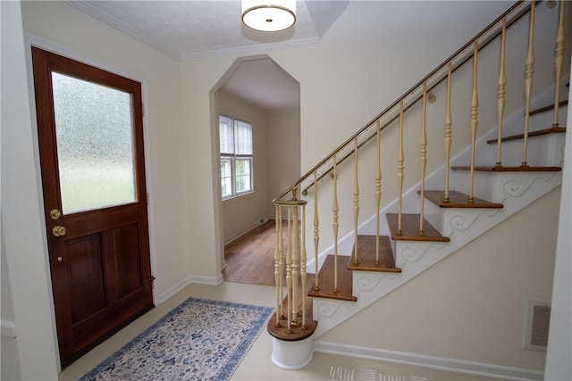 entrance foyer with arched walkways, crown molding, visible vents, stairway, and baseboards