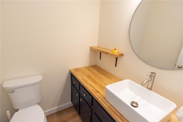 bathroom featuring toilet, baseboards, wood finished floors, and vanity