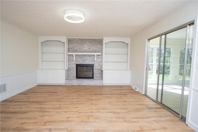 unfurnished living room with built in shelves, a brick fireplace, ornamental molding, and light wood-style flooring