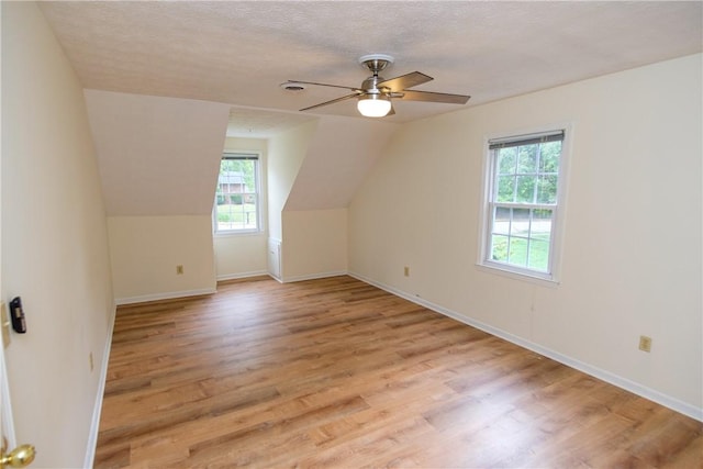 additional living space with light wood-style flooring, baseboards, vaulted ceiling, and a textured ceiling