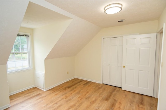 additional living space with light wood-type flooring, visible vents, lofted ceiling, and baseboards