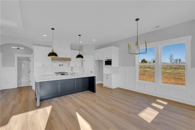 kitchen with arched walkways, light wood finished floors, light countertops, backsplash, and white cabinetry