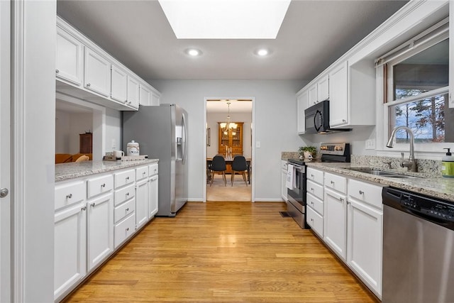 kitchen featuring a skylight, white cabinets, stainless steel appliances, light wood-style floors, and a sink