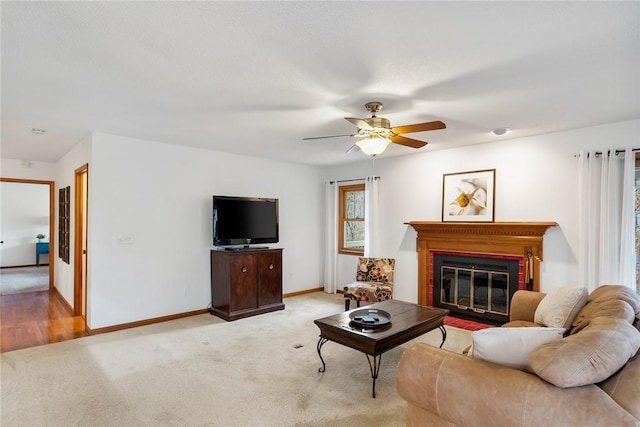 living room featuring ceiling fan, baseboards, light colored carpet, and a glass covered fireplace