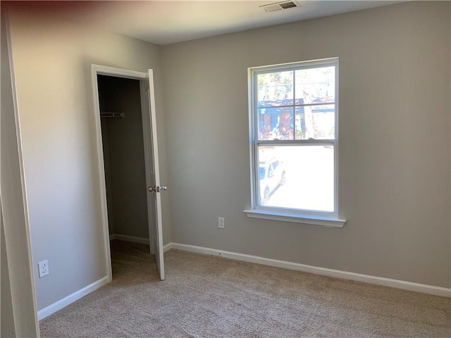 unfurnished bedroom with carpet, a walk in closet, visible vents, and baseboards