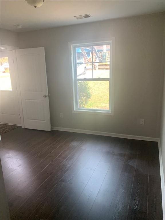 spare room featuring dark wood-style floors, visible vents, and baseboards