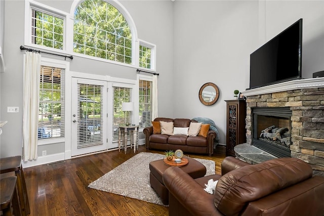 living room with a towering ceiling, visible vents, wood finished floors, and a stone fireplace