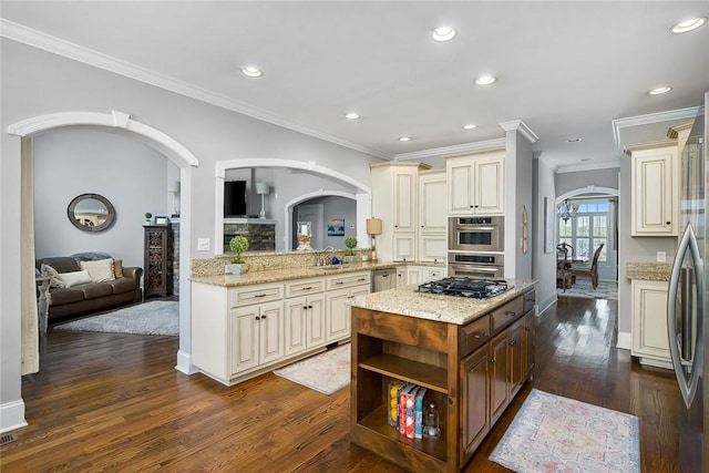 kitchen with stainless steel appliances, arched walkways, cream cabinetry, and light stone counters