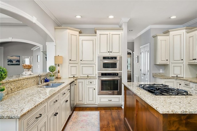 kitchen with light stone counters, dark wood-style flooring, a sink, ornamental molding, and appliances with stainless steel finishes