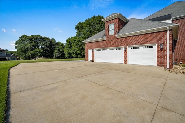 view of side of property featuring a garage, a shingled roof, concrete driveway, and brick siding