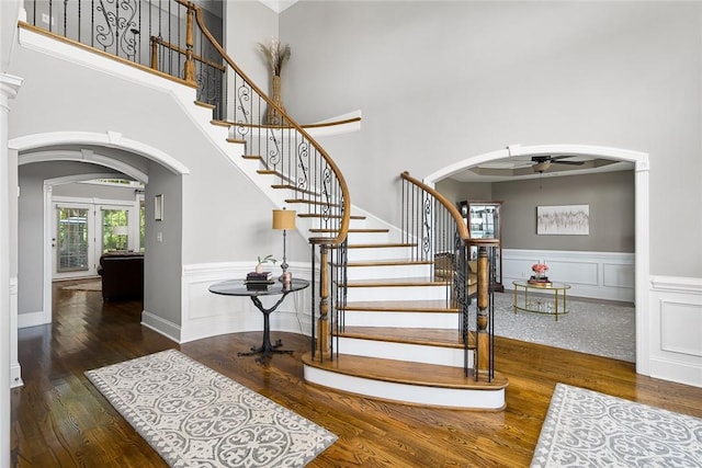 stairway featuring arched walkways, a wainscoted wall, wood finished floors, and a towering ceiling