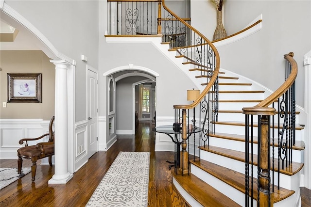 foyer with arched walkways, a wainscoted wall, a decorative wall, wood finished floors, and ornate columns