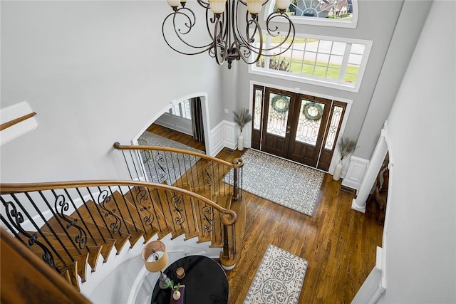 entrance foyer featuring arched walkways, wood finished floors, stairs, a high ceiling, and a notable chandelier