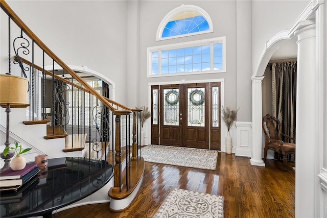 entrance foyer featuring arched walkways, a high ceiling, wood finished floors, stairs, and ornate columns